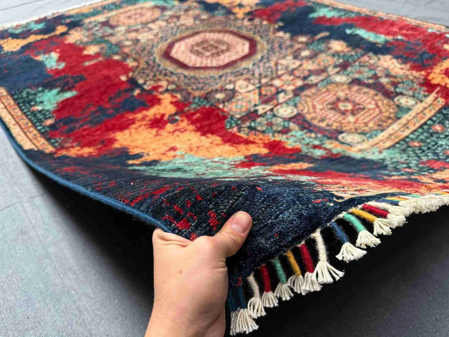 Artisan holding 5x7 handmade wool and silk modern oriental rug in red, teal, and gold