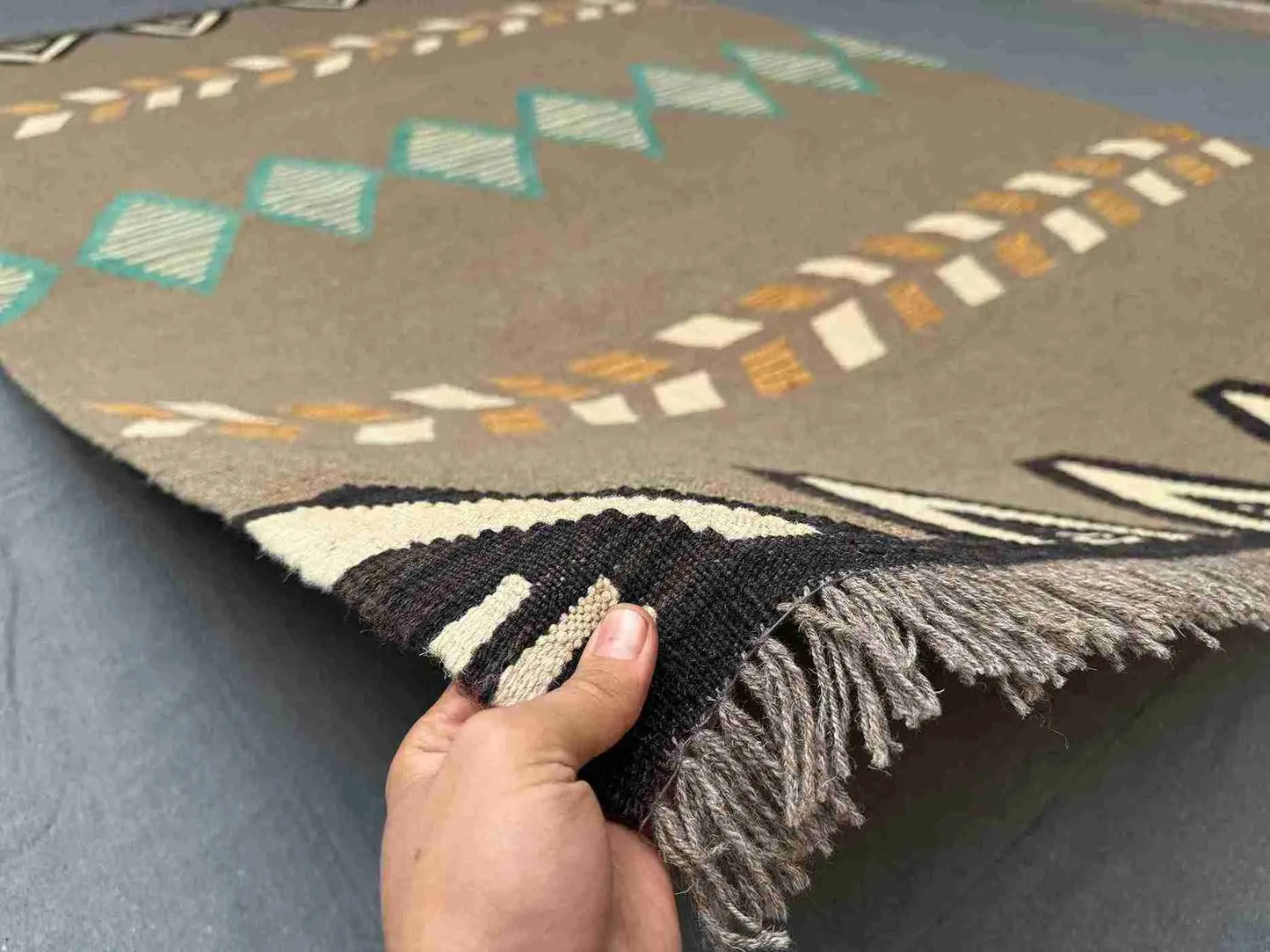 Handmade 6x9 Kilim rug in hand showing geometric pattern and earthy colors.