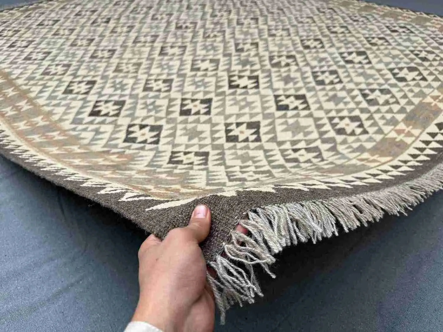 8x10 handmade Turkish Kilim rug held in hands – front view showing geometric wool flatweave in beige and brown.
