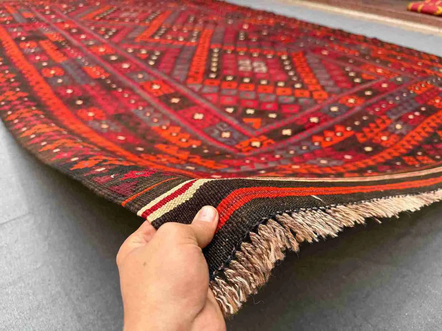 Large 8x12 Turkish Kilim rug in red and black held in hands – front view of handmade wool flatweave.