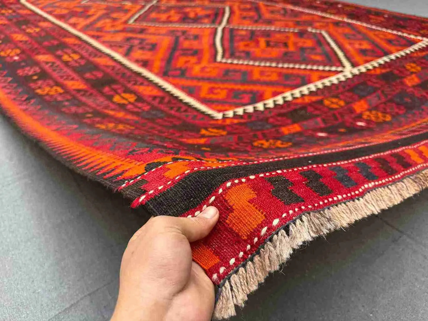 Handmade 8x12 Turkish Kilim rug held in hands – front view of red and black geometric wool flatweave.