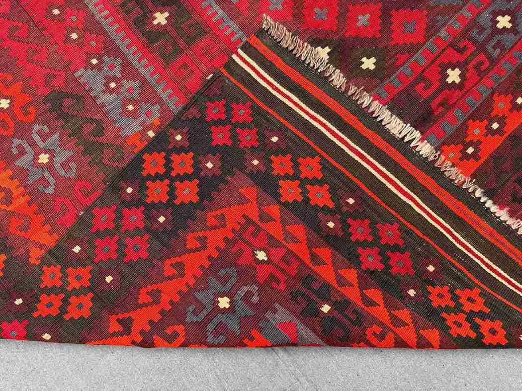 Folded backside of Turkish Kilim rug – hand-knotted wool carpet in red and black tribal pattern.