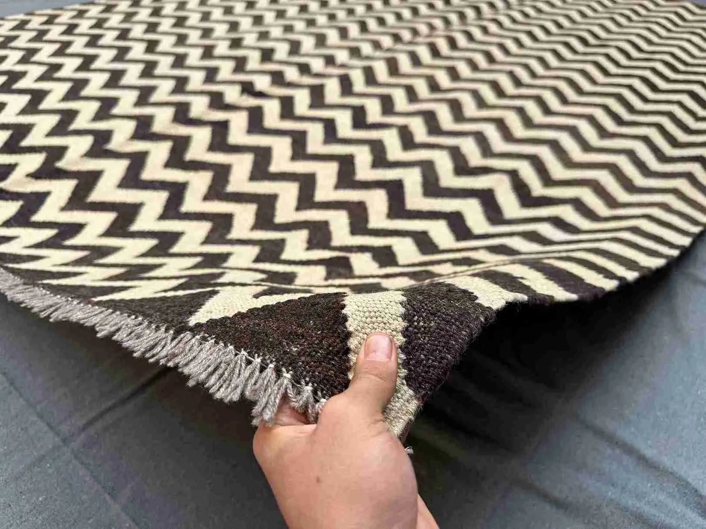Handmade Kilim rug in black and ivory held in hand, flatweave detail
