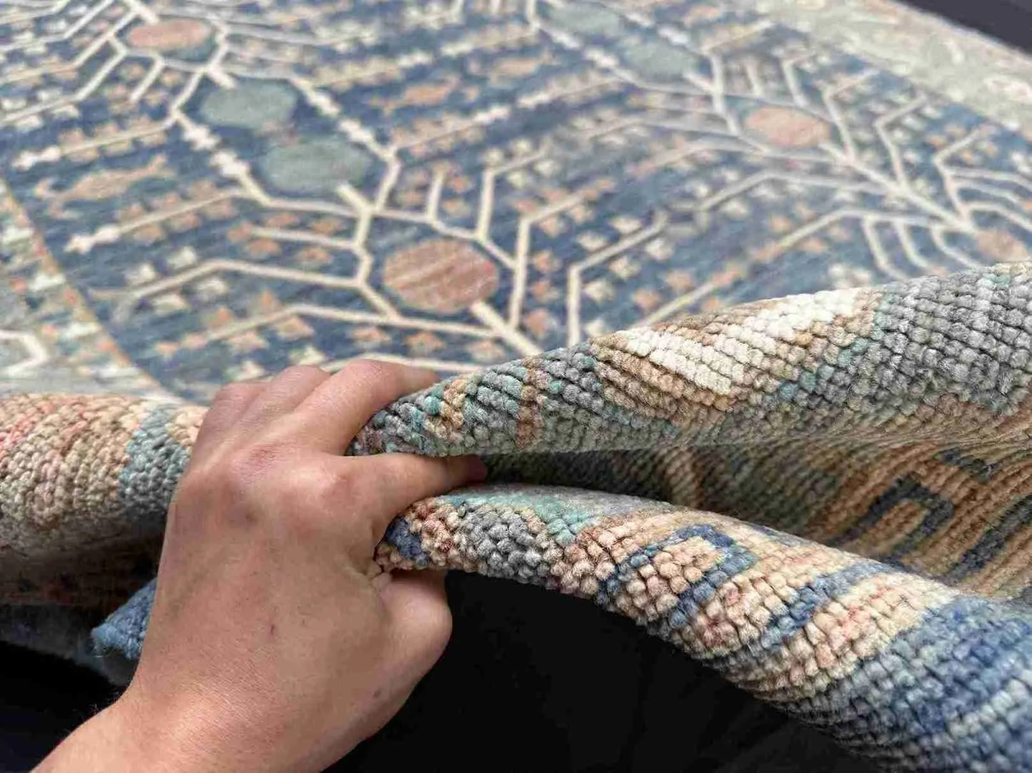 Handmade 5x9 blue and beige wool rug held to show thickness and weave
