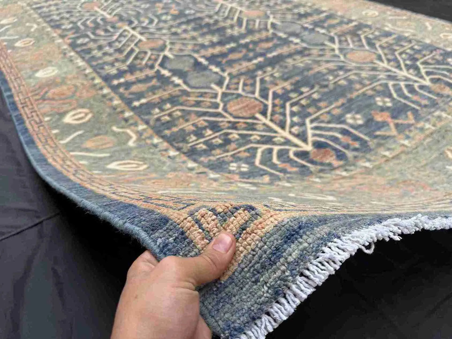 Handmade 5x9 blue and beige wool rug held to show thickness and weave