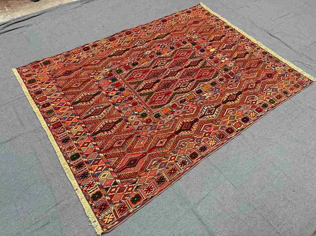 Turkish Afghan kilim rug on floor styled in boho interior with red and orange color palette