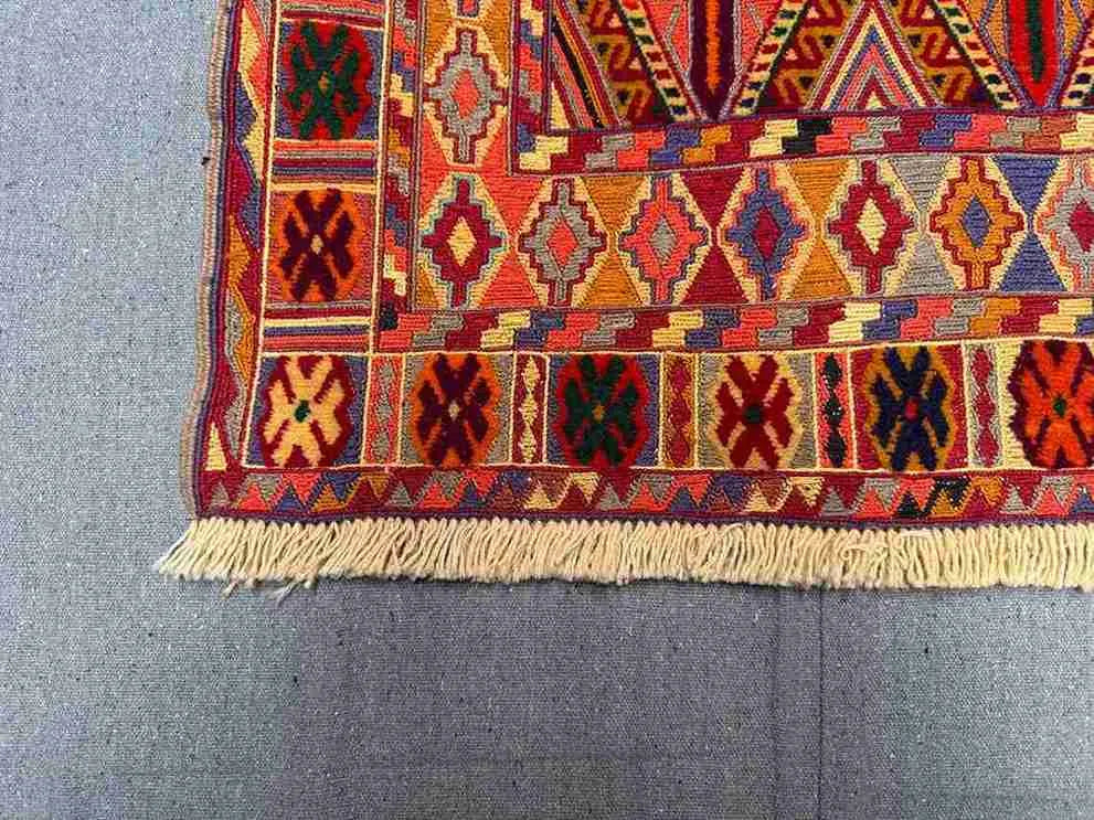 Corner detail of handmade Afghan kilim rug in red, orange, and earthy tones