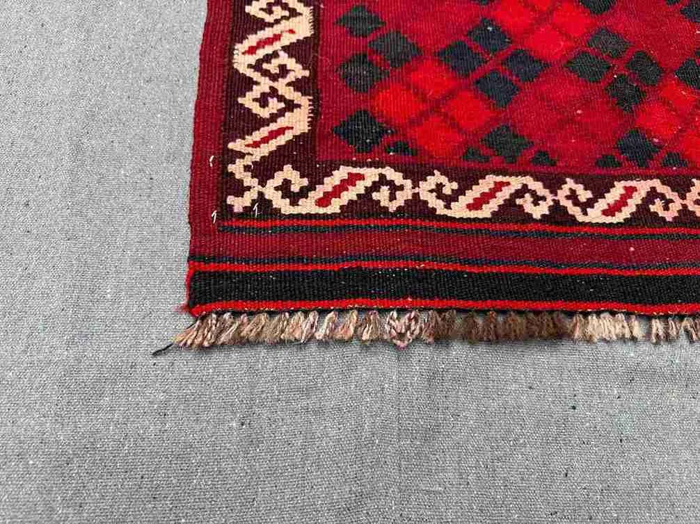 Corner detail of small vintage red Afghan Kilim rug – handmade wool with tribal geometric pattern.