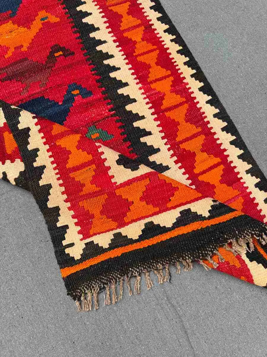 Folded handmade Turkish Kilim rug – red and orange wool flatweave with tribal details.