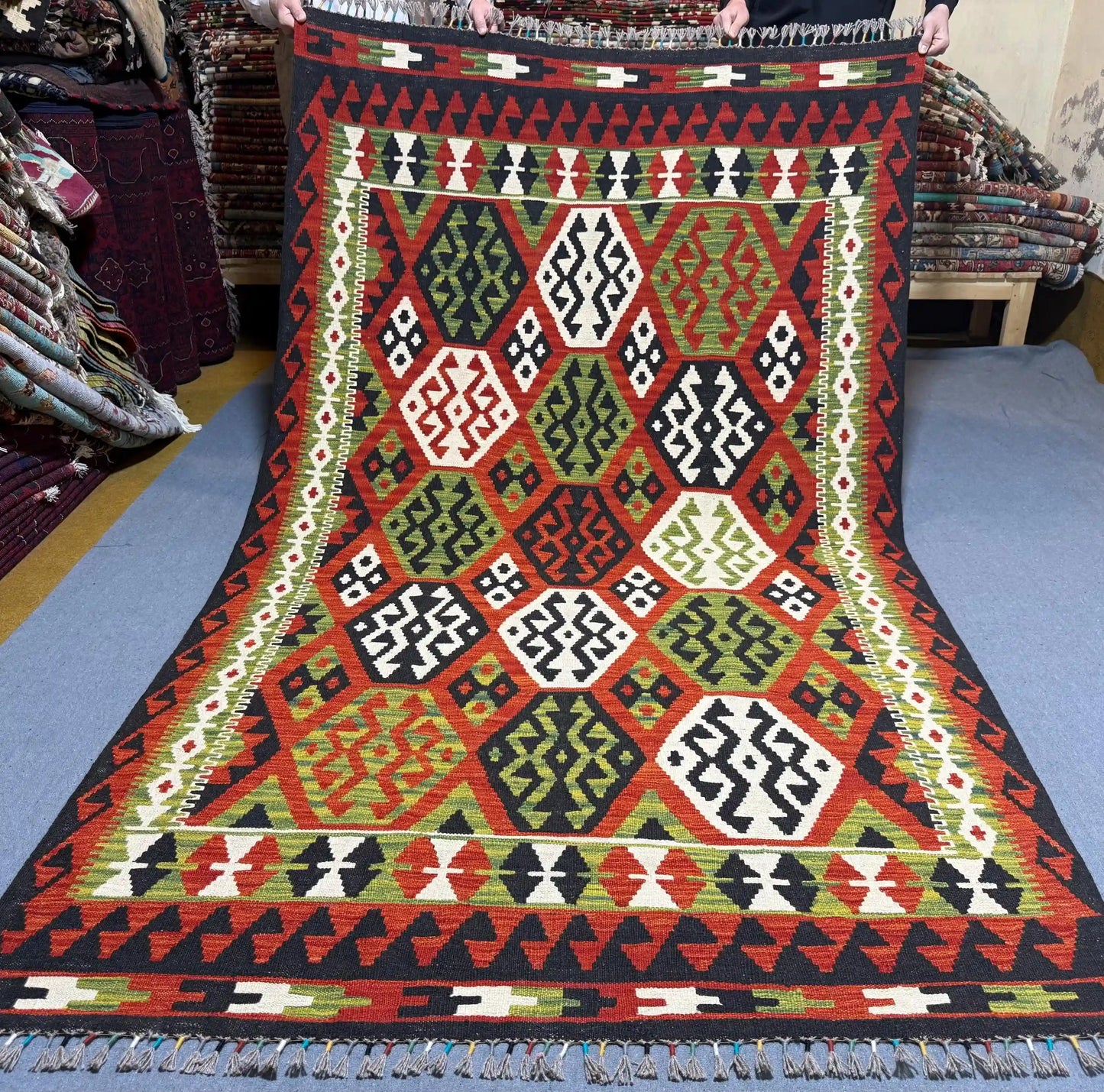 Full overhead view of 5x8 ft Turkish Kilim rug with hexagon pattern in red, green, black, and ivory
