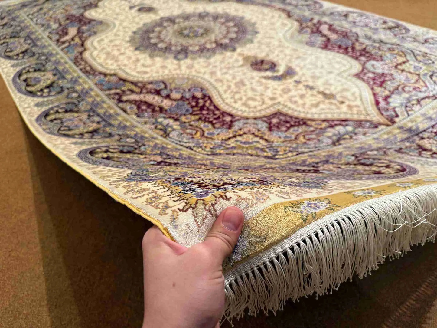 Handmade 5x8 silk rug held in hands showing fine knotted texture