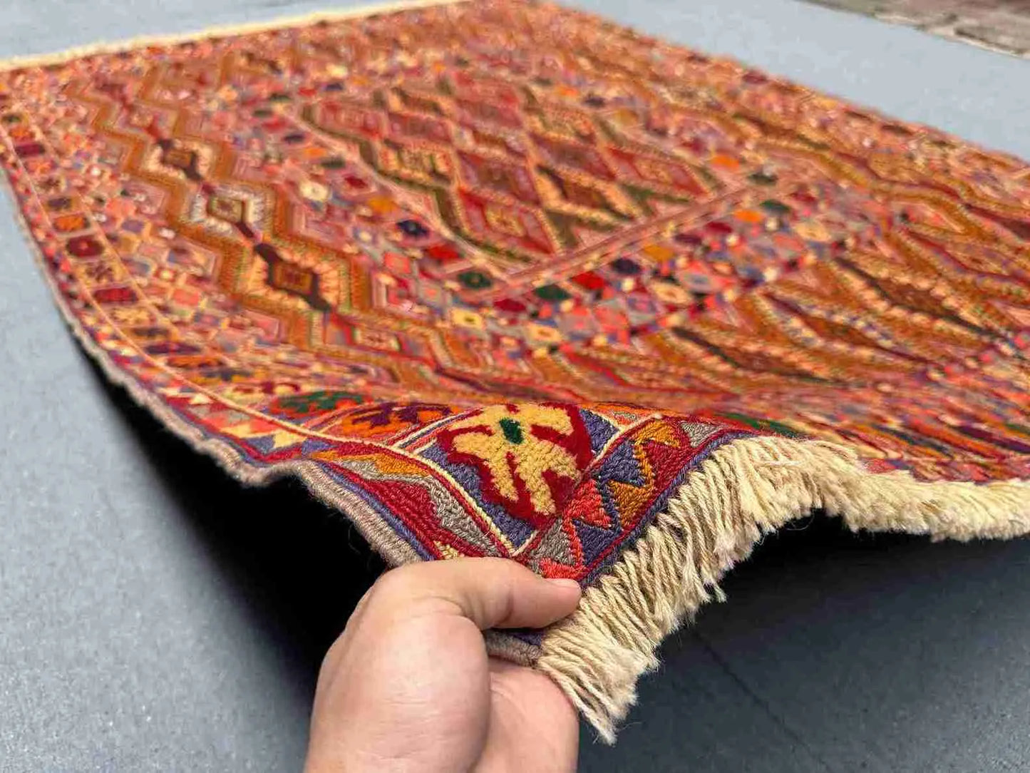 Handwoven 4.9x6.6 Turkish Afghan kilim rug held in hands, showing tribal wool texture and red-orange tones