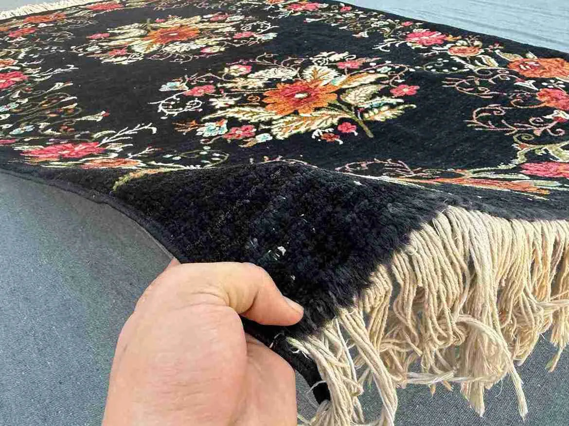 Handmade Karabakh wool rug in hand showing black floral pattern and texture