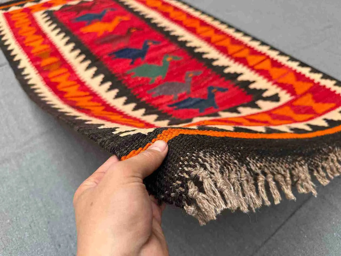 Handmade multicolor Turkish Kilim rug in red and orange tones held in hands – front tribal wool flatweave.