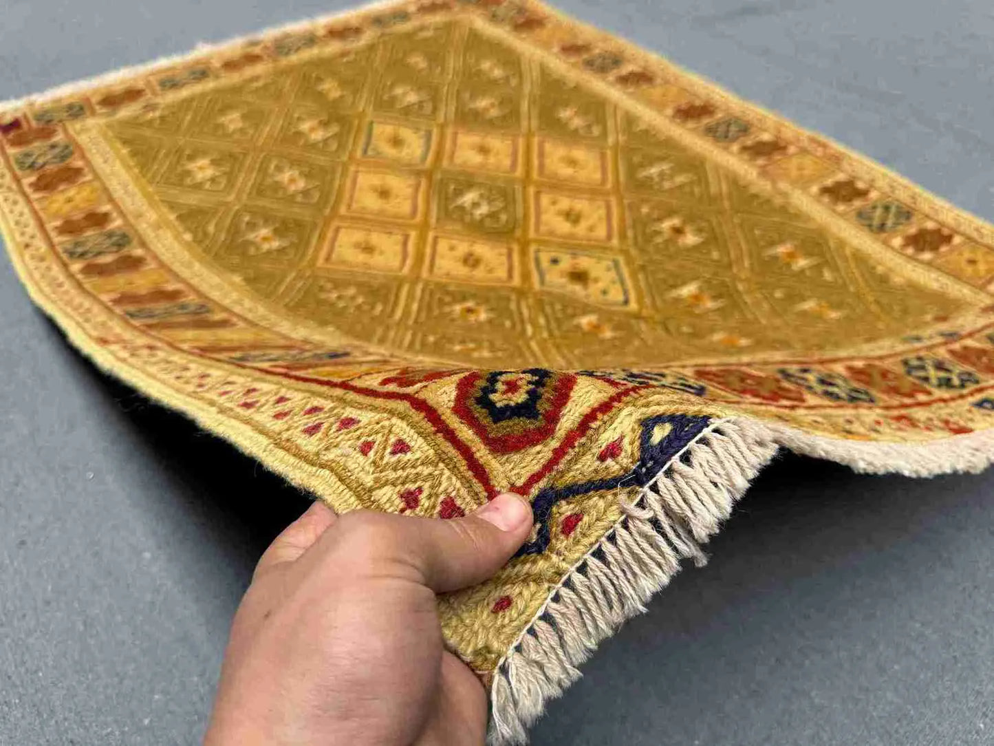 Handmade Afghan kilim rug in hand showing olive and gold wool texture