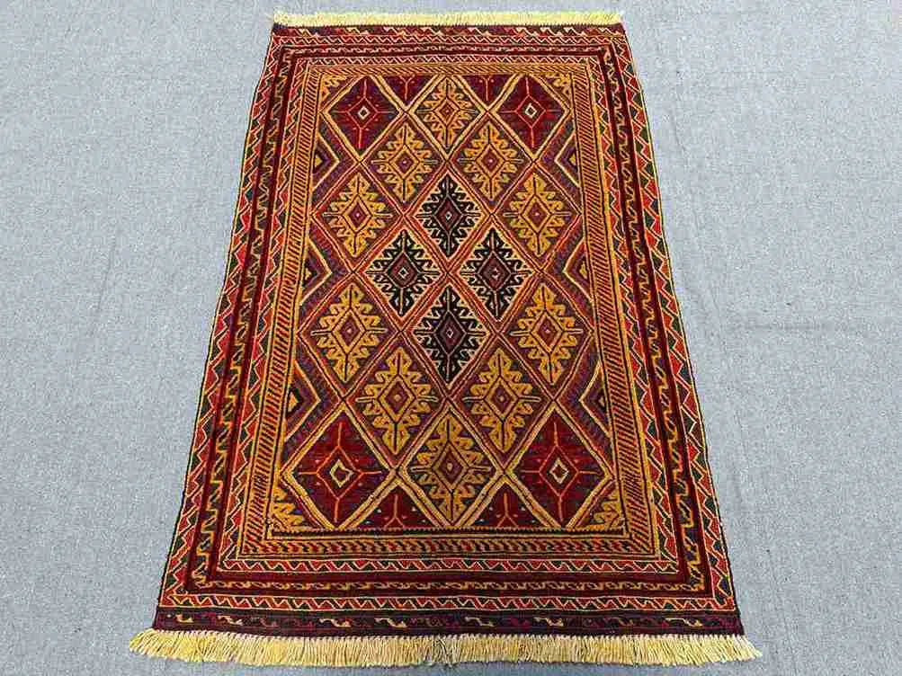 Red and gold Afghan rug styled on wooden floor with bohemian decor