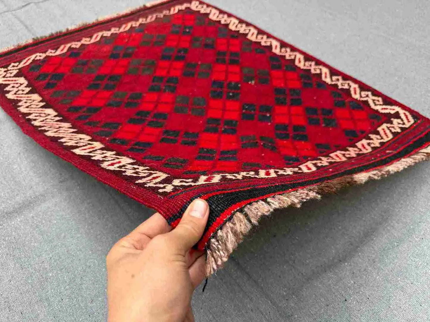 Front view of handmade vintage red Afghan Kilim rug held in hands – small geometric wool flatweave.