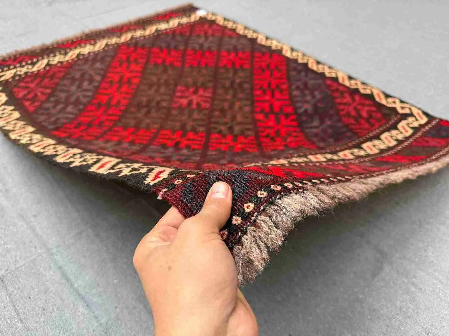 Handwoven small Afghan red Kilim rug held in hands – front view showing geometric wool flatweave.