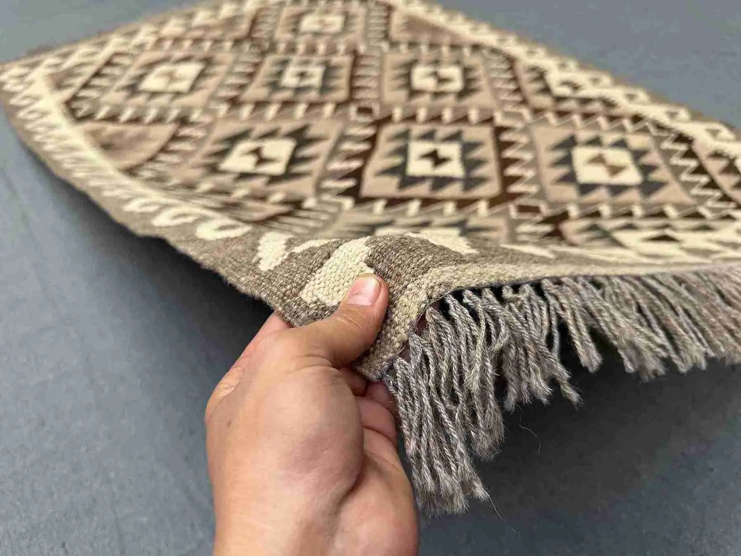 Handmade small Turkish Kilim rug held in hands – front view showing tribal wool flatweave pattern.