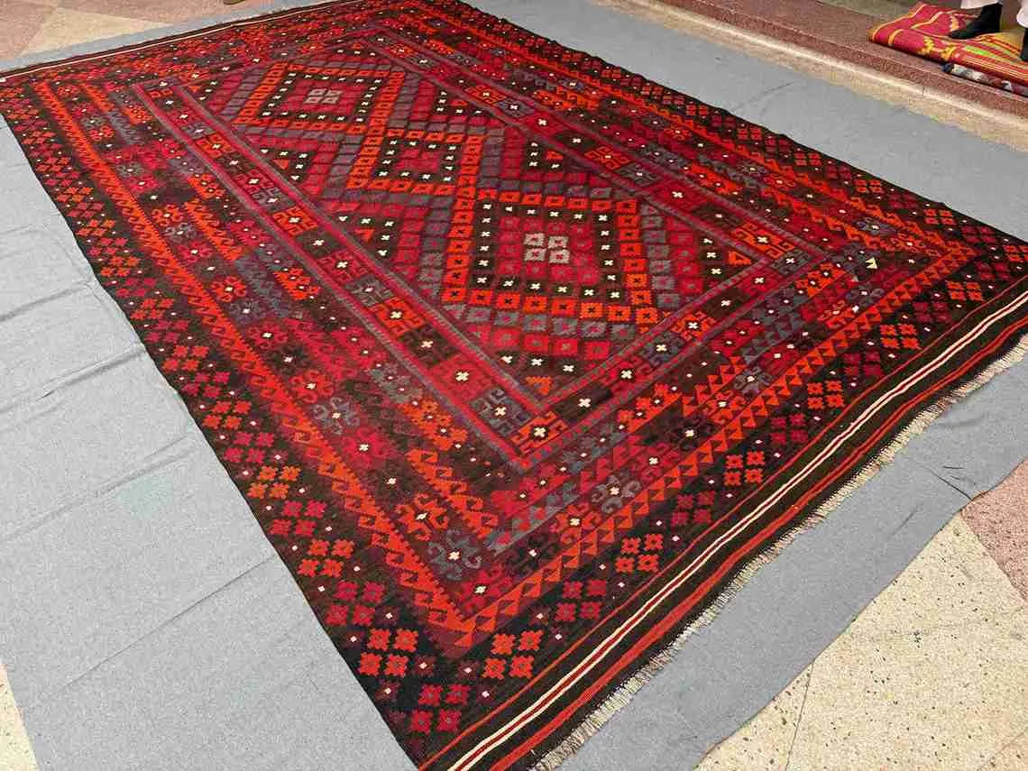 Traditional Turkish Kilim rug in red and black on wooden floor – large 8x12 handmade wool area carpet.