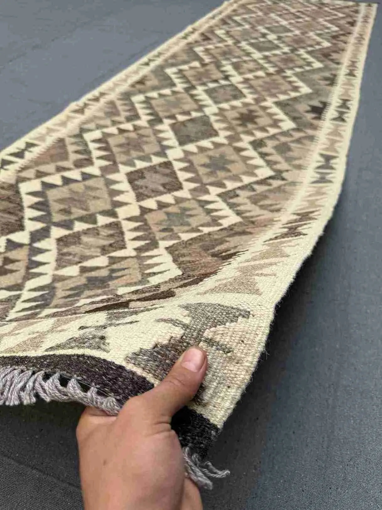 Handmade Turkish Kilim runner rug in hands – showcasing front wool texture in neutral tones.