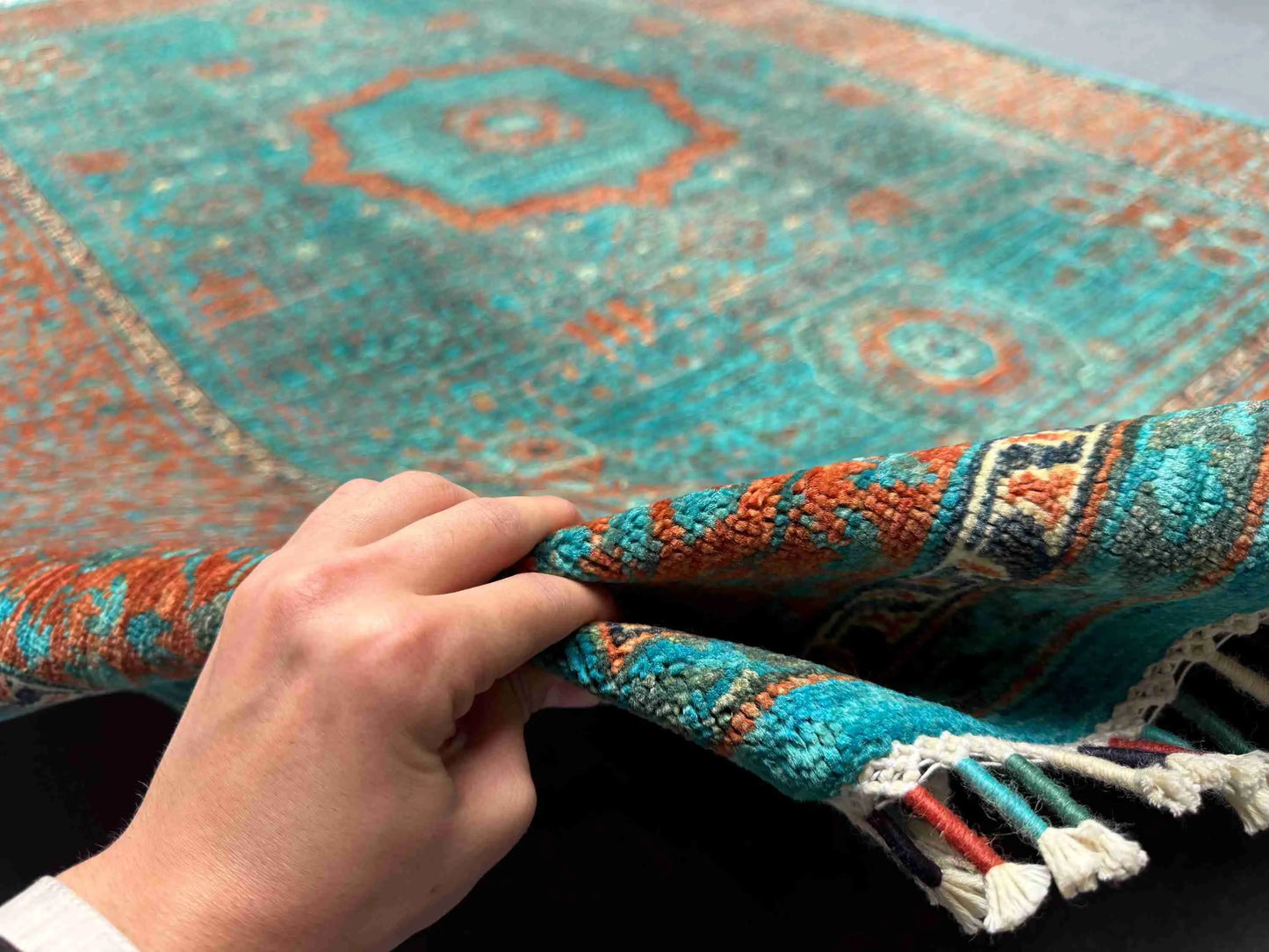Hand-knotted 6x8 turquoise Mamluk wool rug held for close texture view