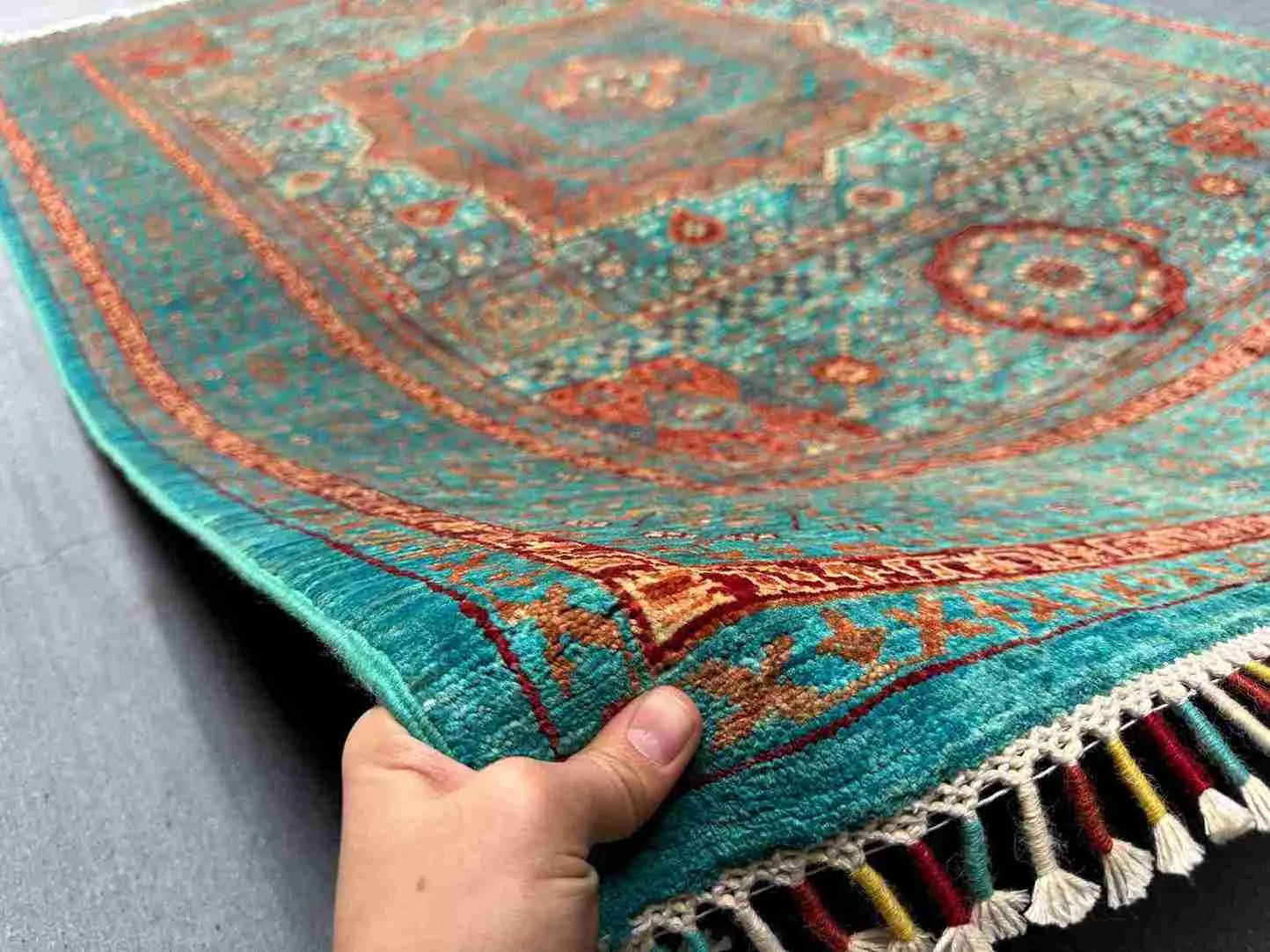 Handmade Mamluk rug in hand showing turquoise, red, and green wool pattern