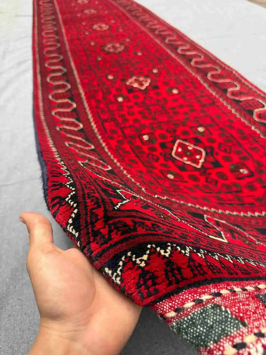 Handmade red 3x12 Khal Mohammadi runner rug held in hand showing tight wool weave