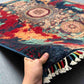 Artisan holding 5x7 handmade wool and silk modern oriental rug in red, teal, and gold