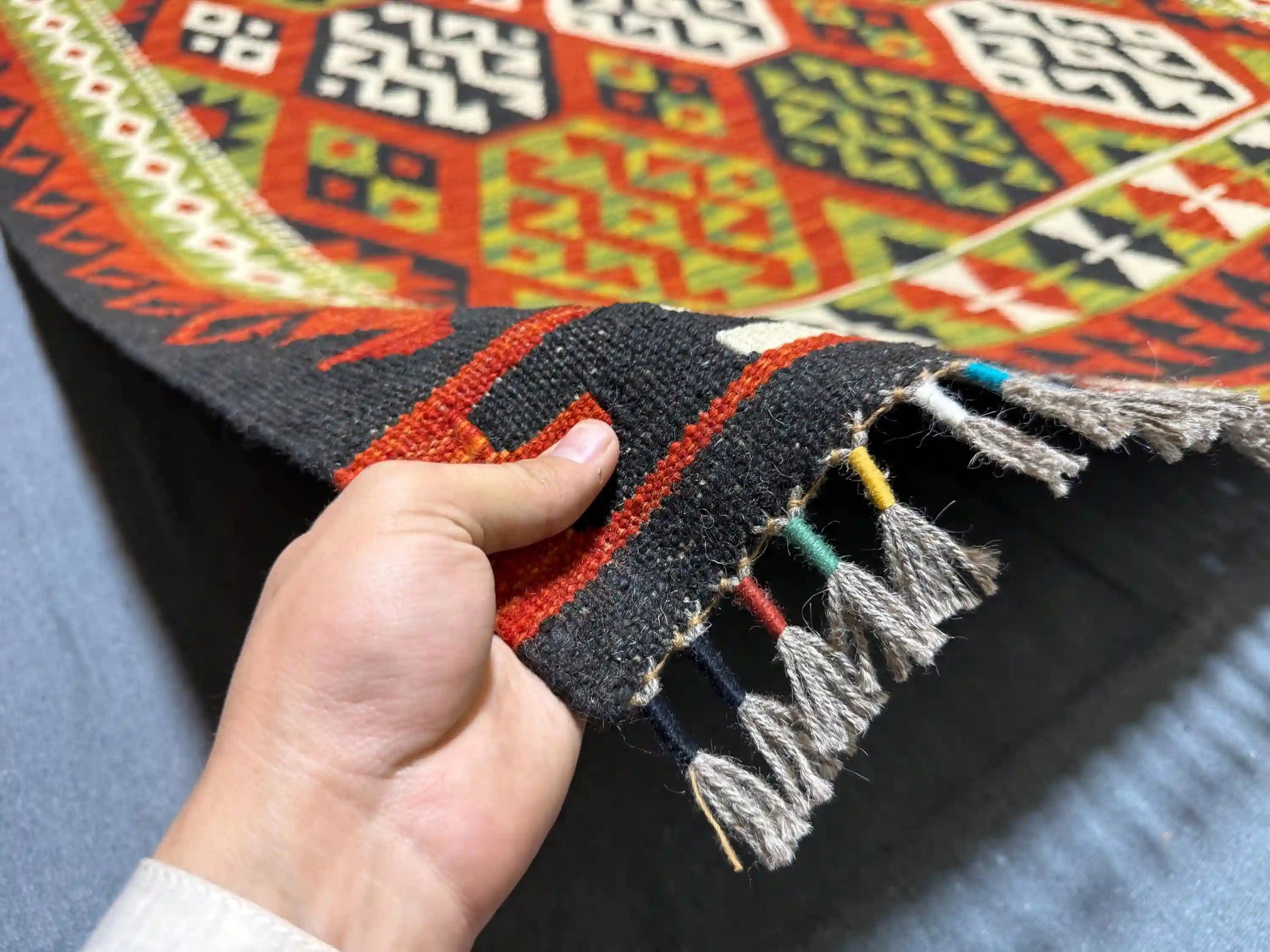 Person holding a 5x8 ft handmade Turkish Kilim rug showing tribal hexagon pattern in red, green, black, and ivory