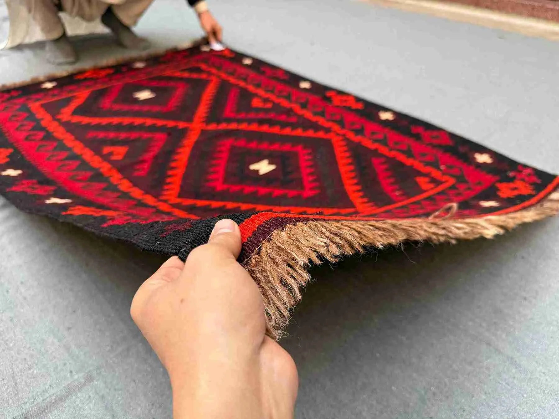 Front view of 5x8 handmade vintage Turkish Kilim rug held in hands – red and black tribal wool flatweave.