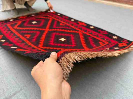 Front view of 5x8 handmade vintage Turkish Kilim rug held in hands – red and black tribal wool flatweave.