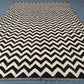 Full view of black and ivory handmade Kilim rug on wooden floor