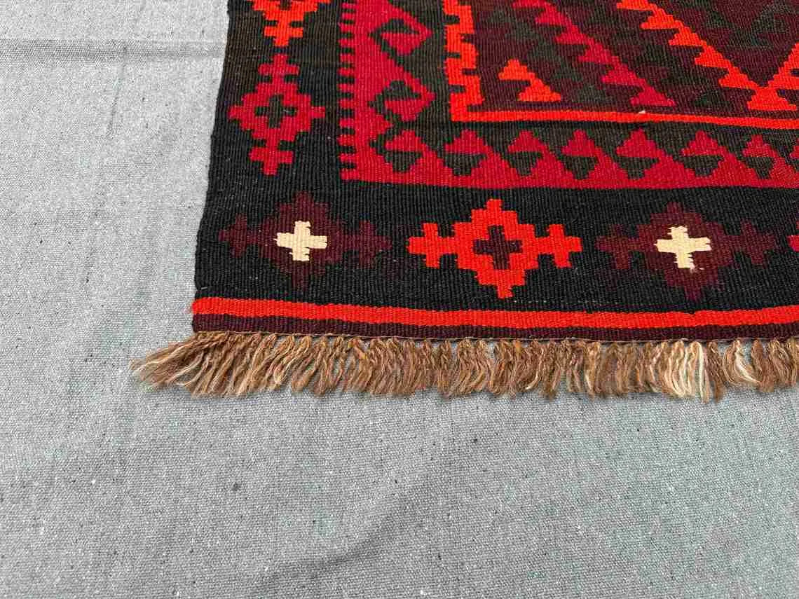 Corner detail of Turkish Kilim rug – handwoven red and black wool flatweave with tribal design.