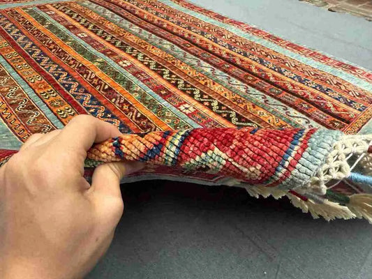 Handmade vintage Turkish kilim rug held in hands showing floral and stripe design