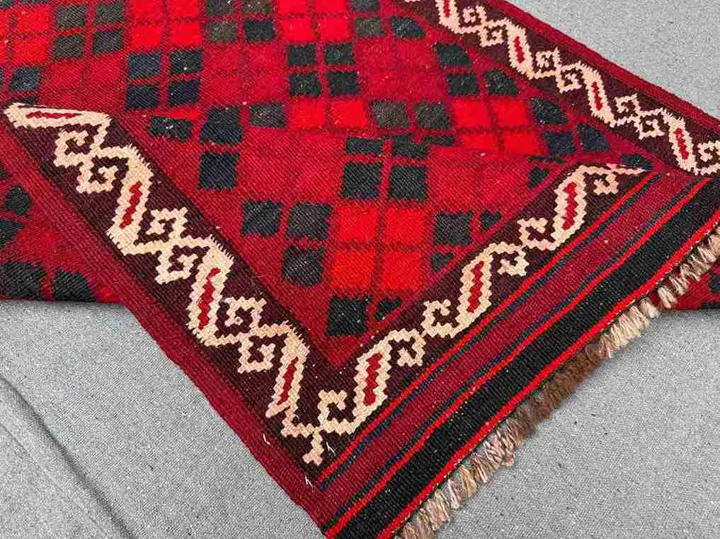 Folded view of small Afghan Kilim rug – handmade red wool flatweave with tribal motifs.