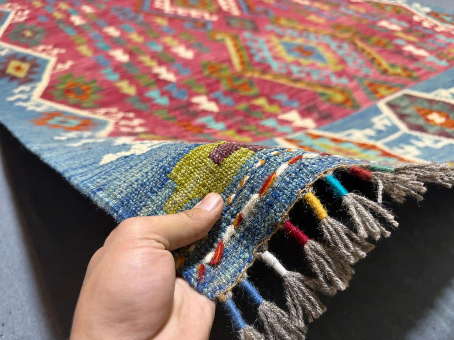 Authentic handmade 5x8 Turkish Kilim rug in hands showing texture and craftsmanship.