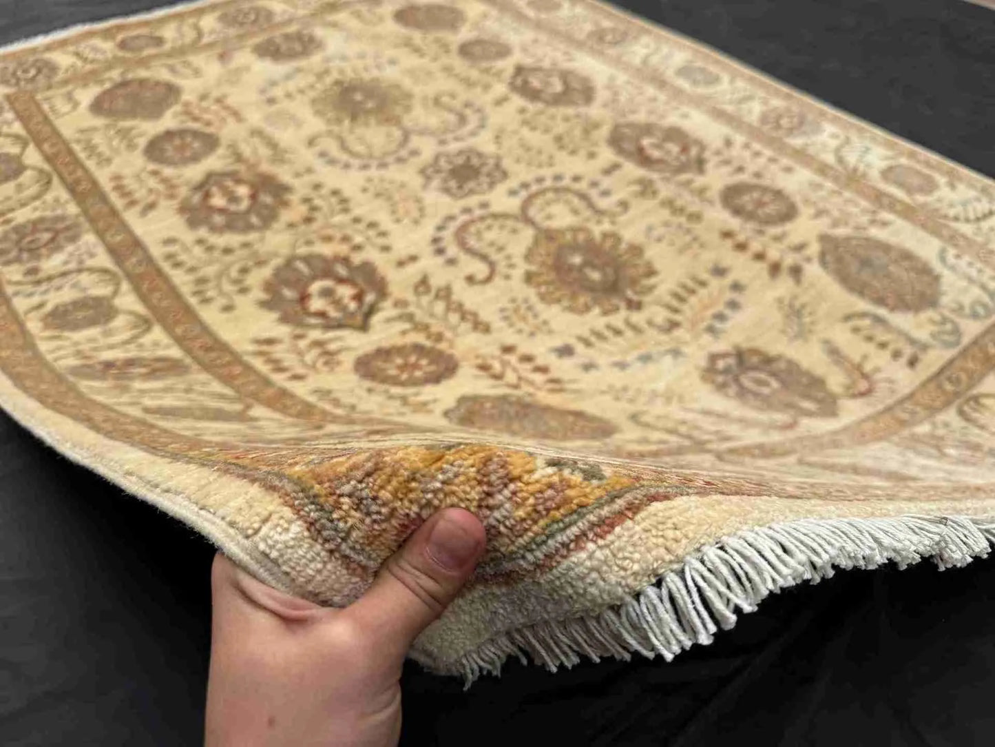 Authentic handmade ivory floral Chobi rug 5x7 ft shown in hands – soft beige wool Persian-style carpet.