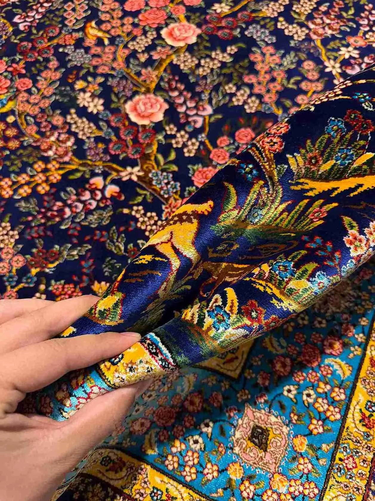 Luxury silk rug with floral and deer motifs held in hand for detail