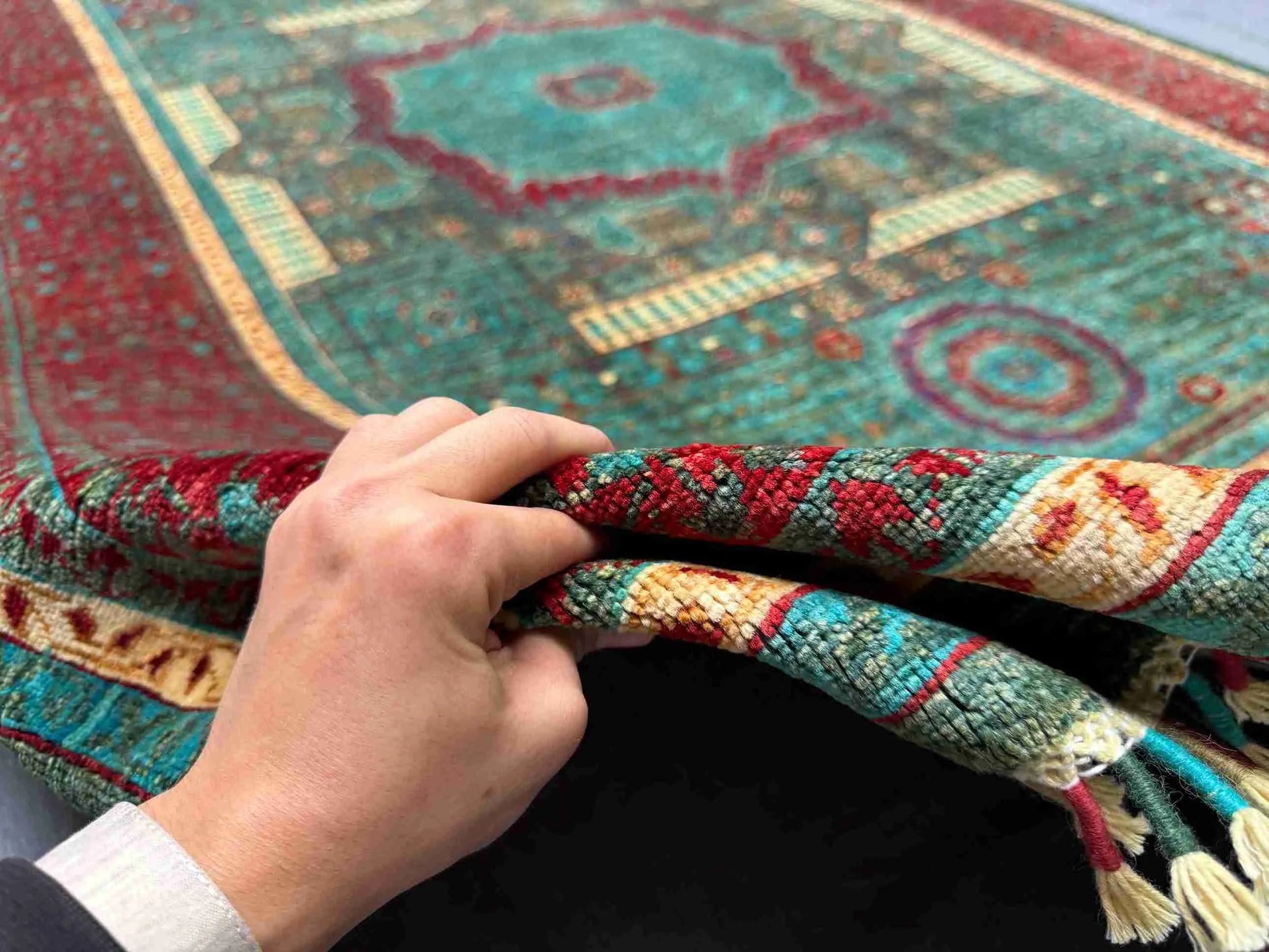 Knotted wool Oriental rug in red and teal displayed in-hand