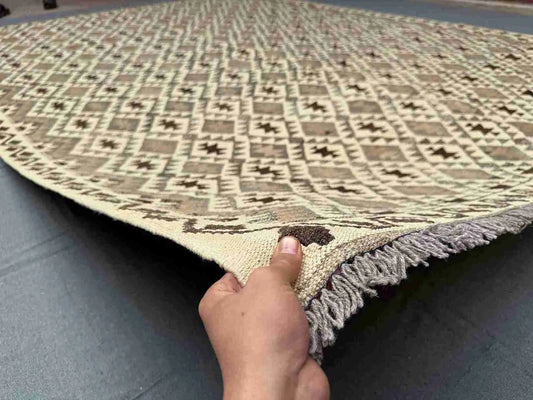 Handmade Turkish Kilim rug held in hands – front view showing earthy beige and brown geometric flatweave.