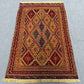Red and gold Afghan rug styled on wooden floor with bohemian decor