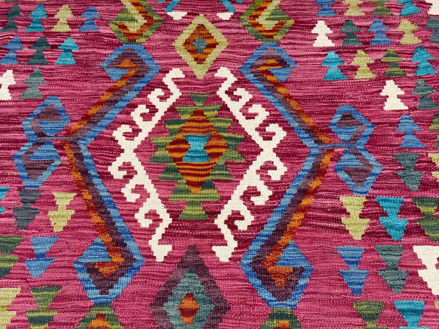 Close-up of tribal geometric patterns on Turkish Kilim rug in pink, blue, and green