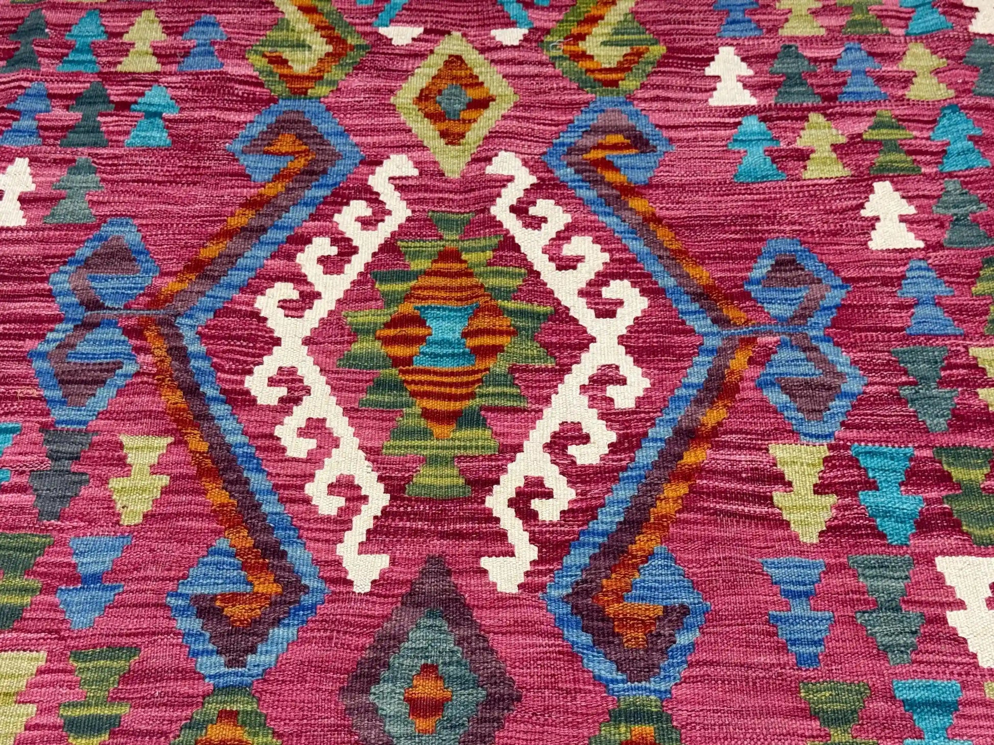Close-up of tribal geometric patterns on Turkish Kilim rug in pink, blue, and green