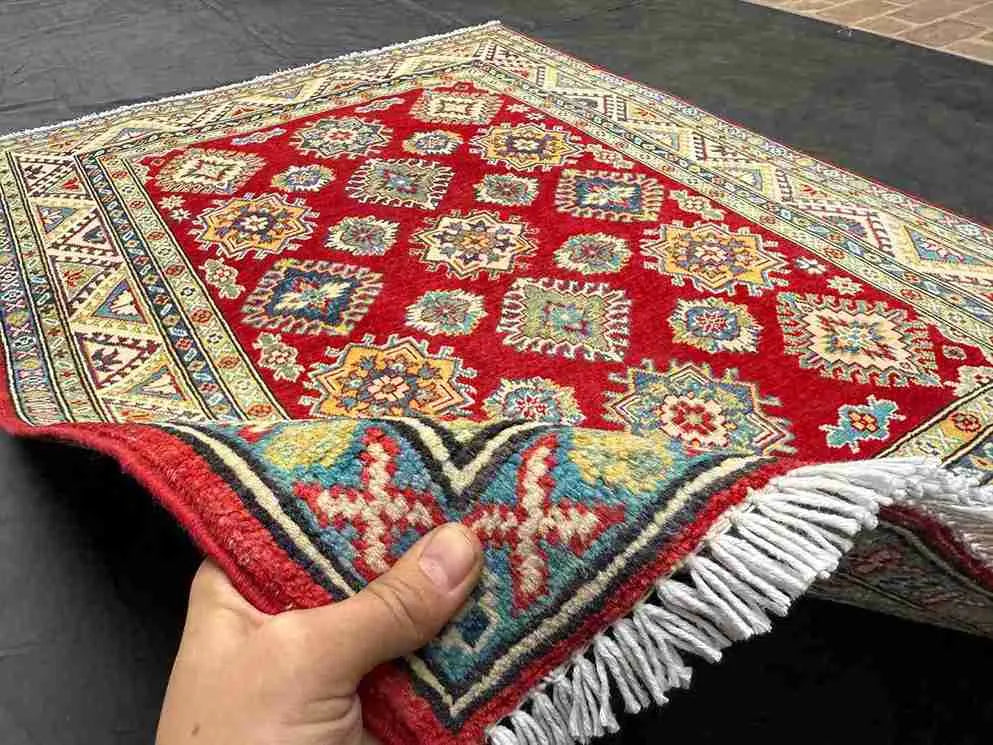 Artisan holding a 5x7 ft red & beige Turkish Kazakh wool rug – knotted luxury carpet
