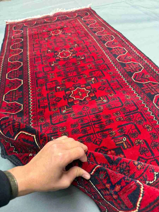 Close-up view of 3x6 ft red handmade runner rug held to show wool texture and tribal knots.