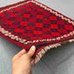 Front view of handmade vintage red Afghan Kilim rug held in hands – small geometric wool flatweave.
