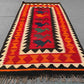 Traditional tribal Kilim rug laid flat on floor – handmade wool rug in warm red-orange hues.