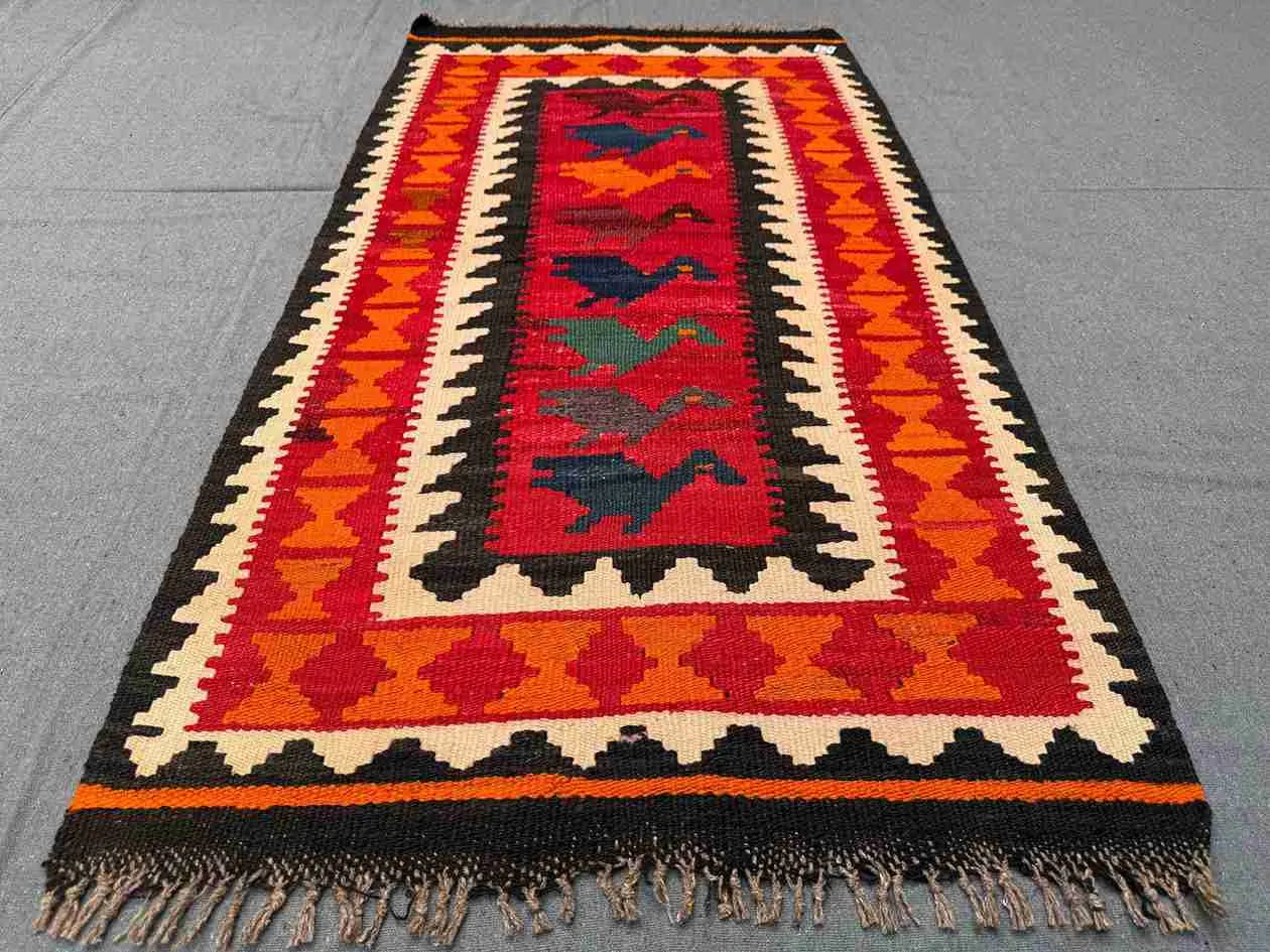 Traditional tribal Kilim rug laid flat on floor – handmade wool rug in warm red-orange hues.