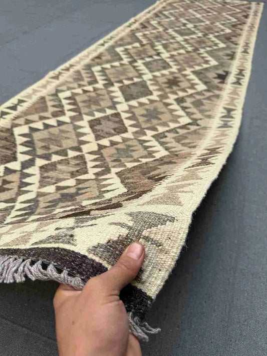 Handmade Turkish Kilim runner rug in hands – showcasing front wool texture in neutral tones.